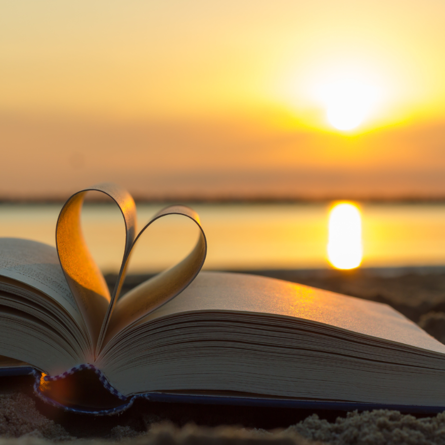Open book resting on sand at sunset with pages folded into a heart shape